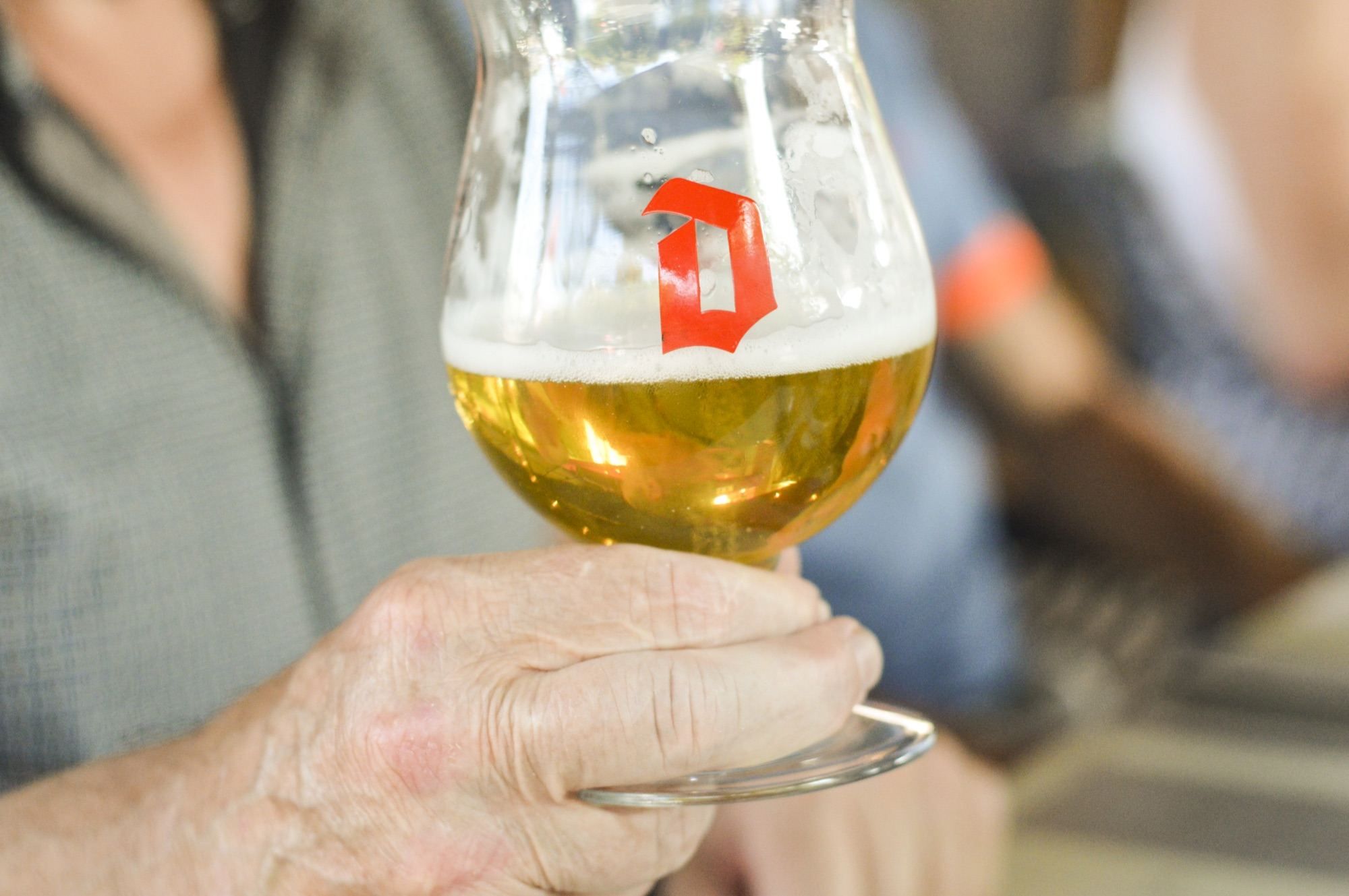 Een glas blond bier in de hand op het zonnige terras