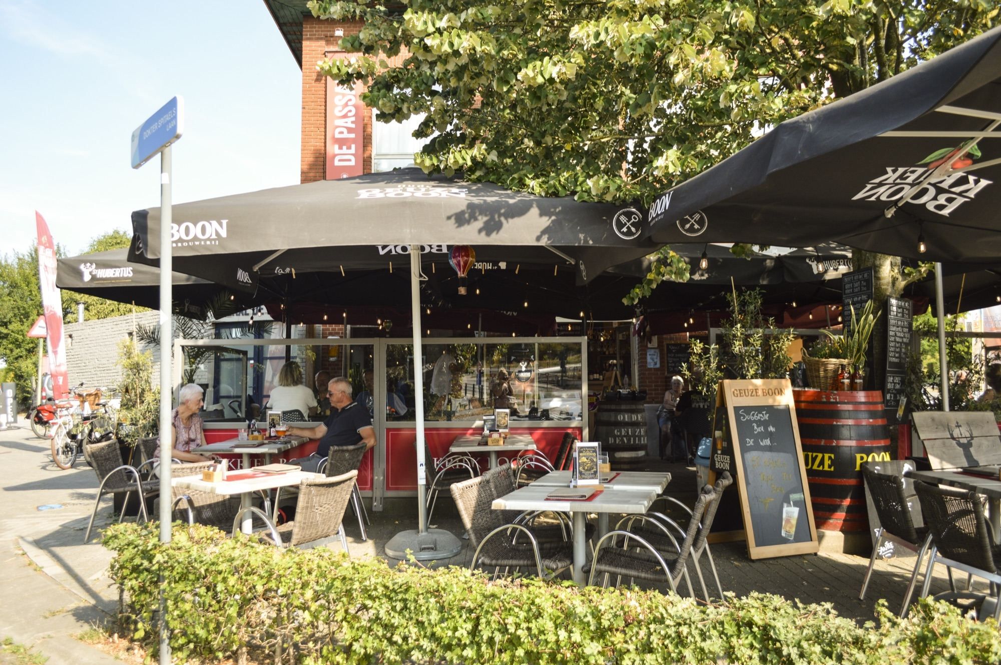 Het terras van De Passant met parasols onder de grote boom